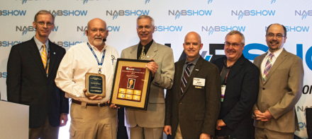 Wayne Pecena (second from left) receives a plaque from Radio World Editor-in-Chief Paul McLane (far right) at the 2015 Ennes Workshop at the NAB Show.